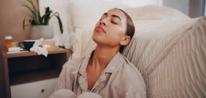 Woman experiencing allergy fatigue resting in bed with medication on nightstand